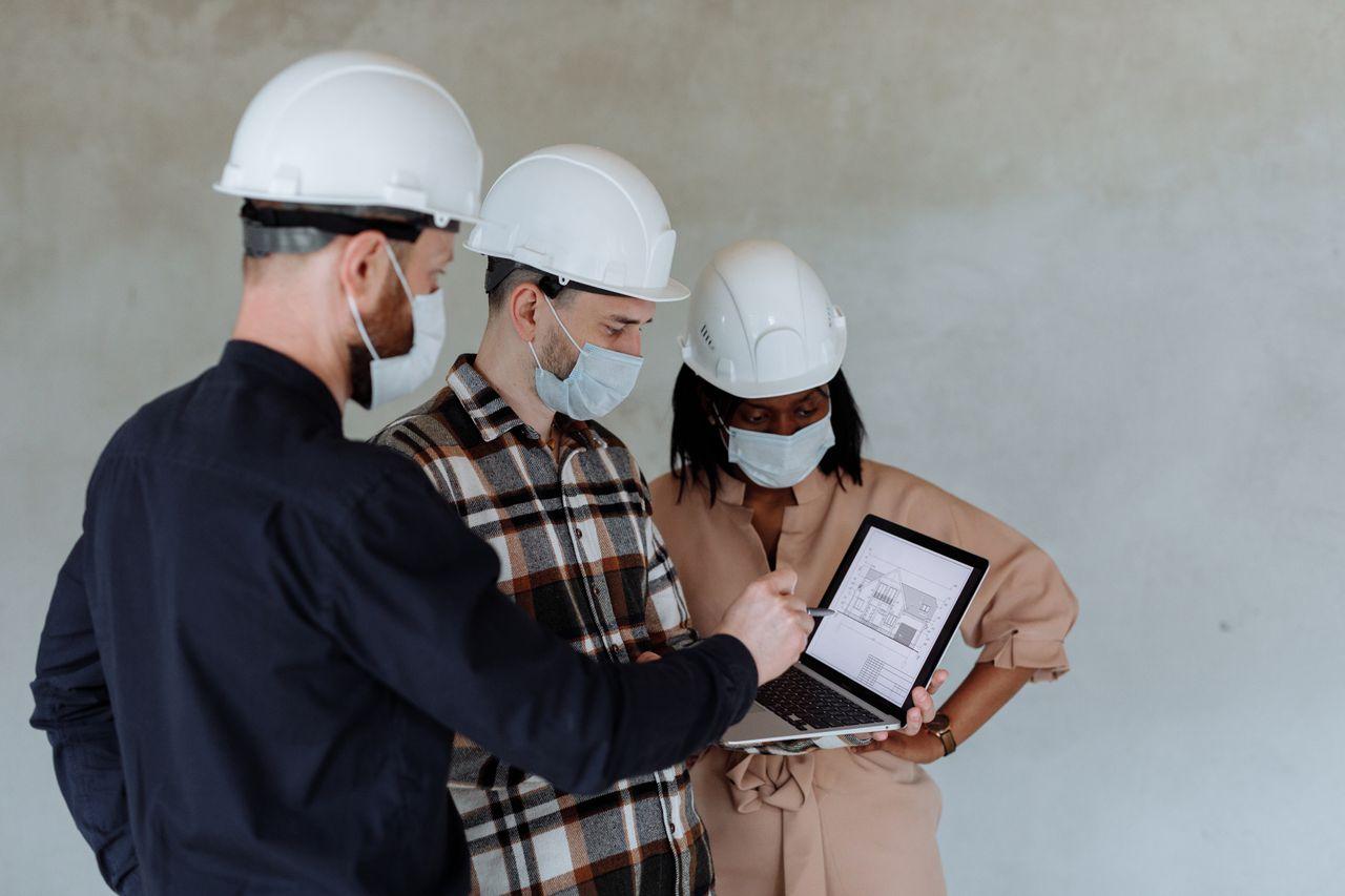 Group of diverse architects with safety gear examining building plans on a laptop